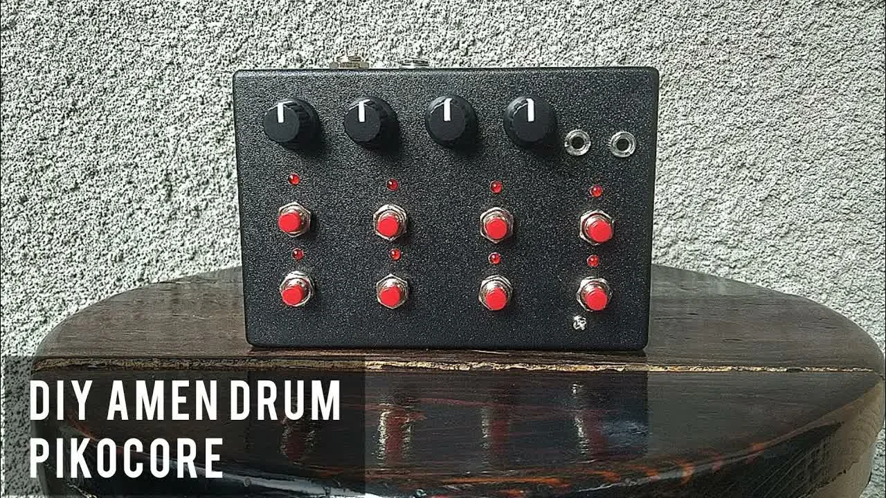 A DIY AMEN DRUM Pikocore held in one hand, with exposed red circuit board, knobs, and eight buttons