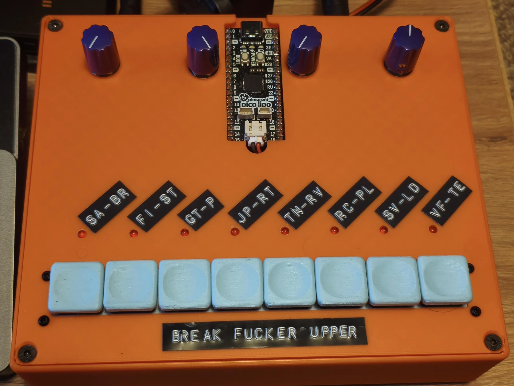 The orange 3D-printed Break Fucker Upper Pikocore with a Pico LiPo, four purple knobs, and eight pale blue buttons